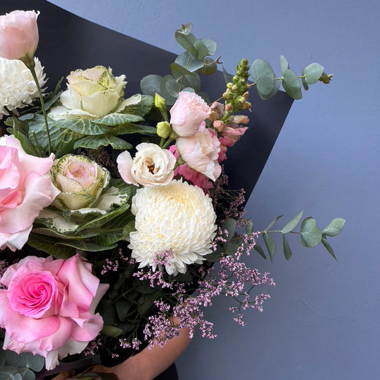 Bouquet of flowers with pink and white roses on a dark surface against a blue wall.