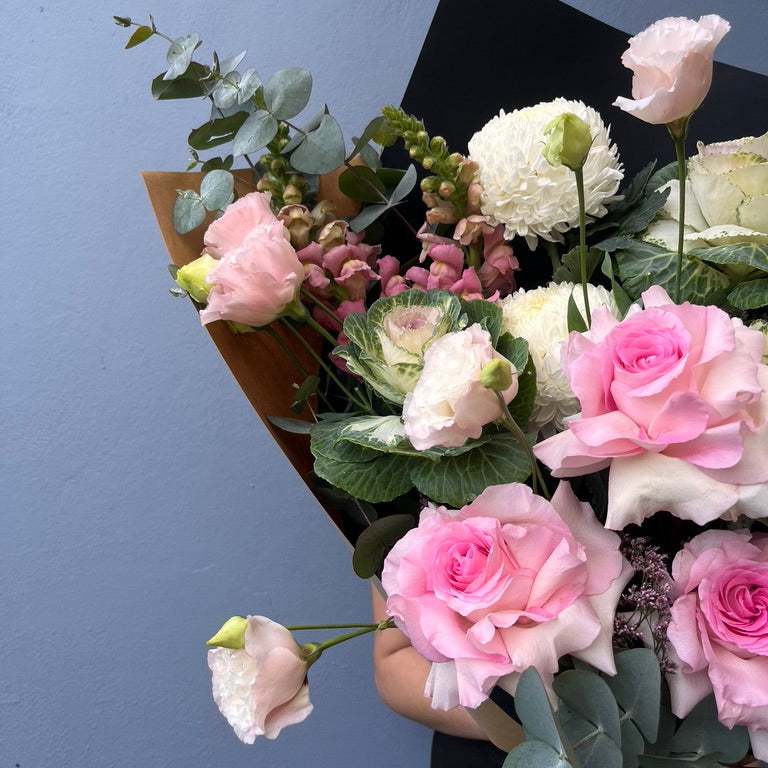 Bouquet of pink and white roses with greenery against a blue background