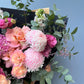Bouquet of pink and peach flowers with greenery against a light blue wall