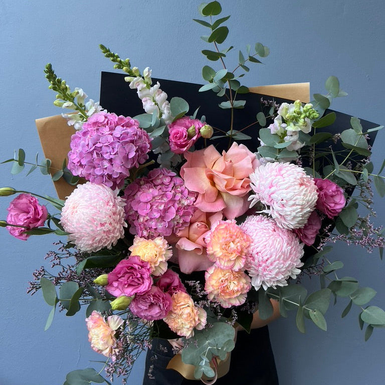 Bouquet of pink and white flowers with greenery against a blue background