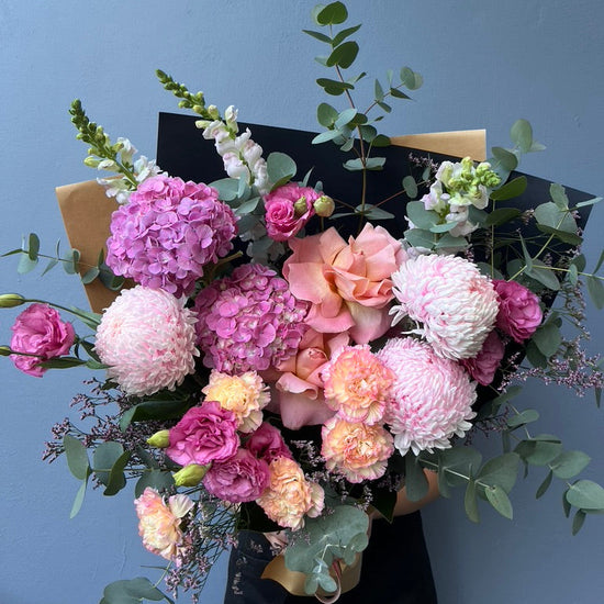 Bouquet of pink and white flowers with greenery against a blue background